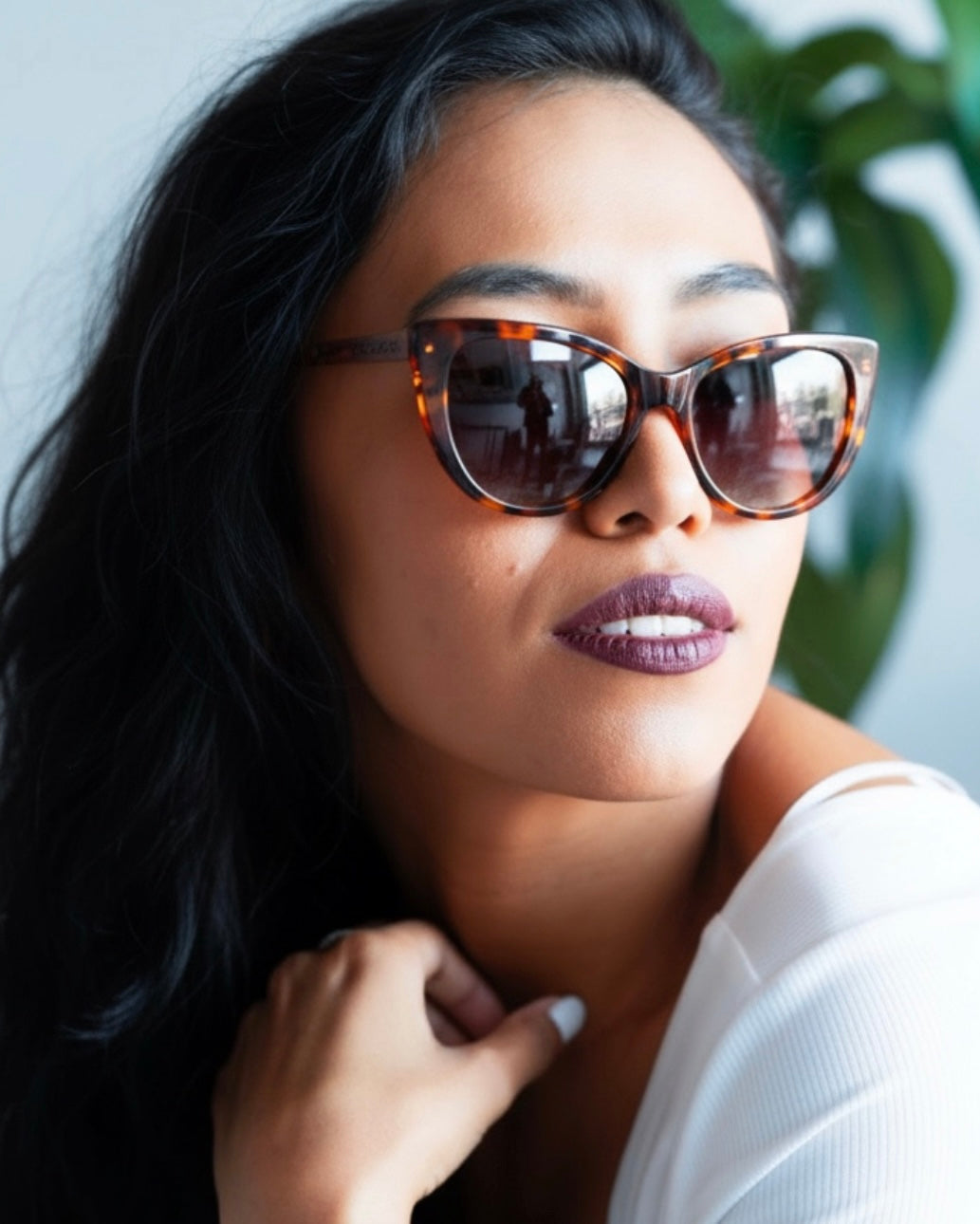 Woman wearing tortoiseshell sunglasses with a blurred plant in the background