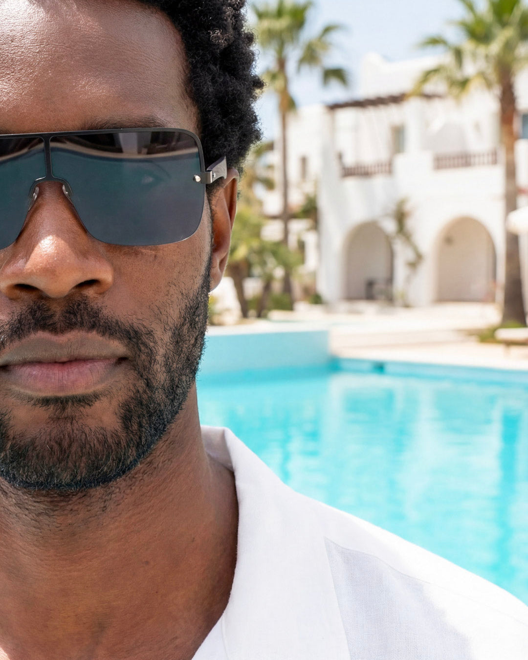 Man wearing sunglasses with a pool and palm trees in the background