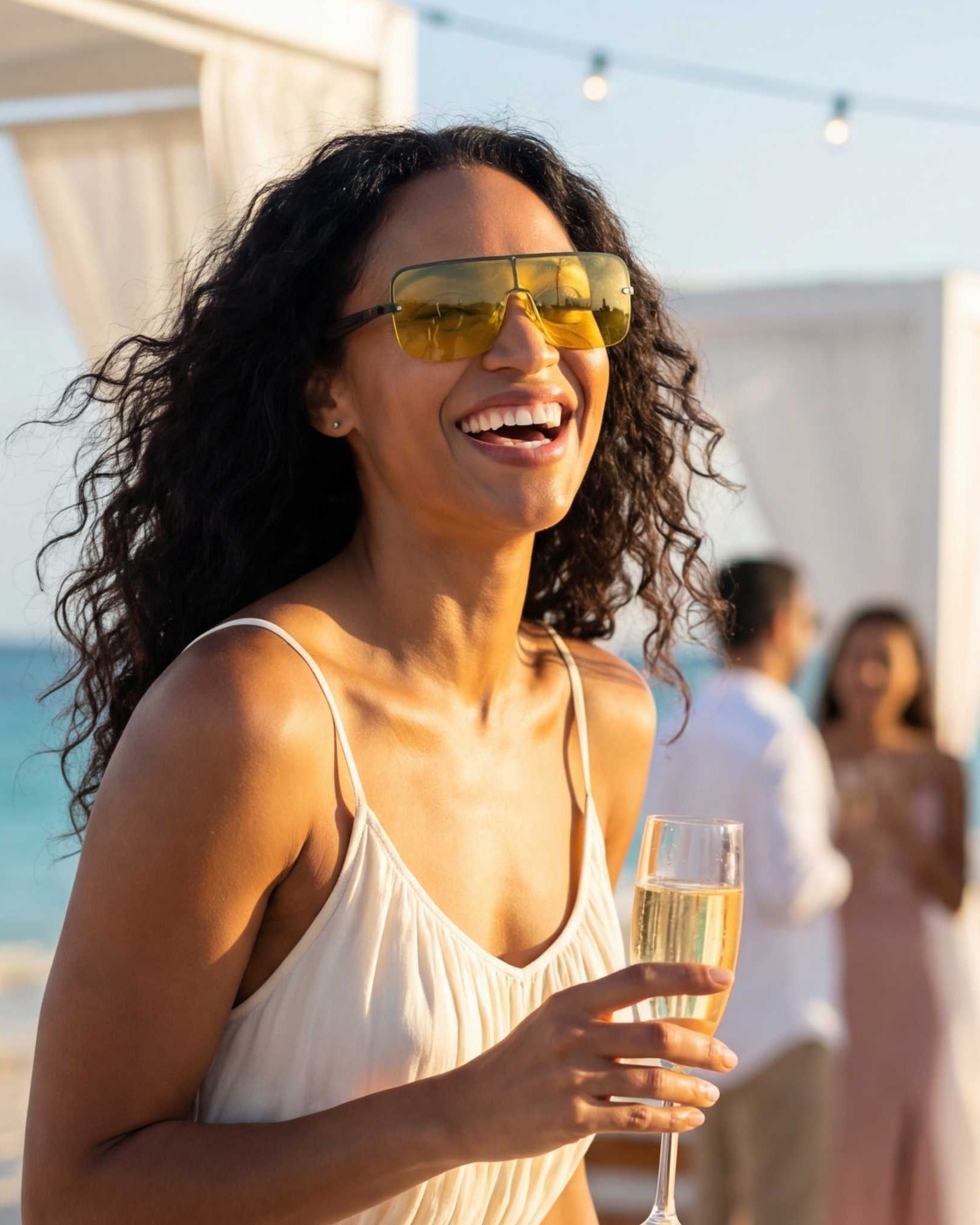 Woman on a beach holding a glass of champagne with people in the background
